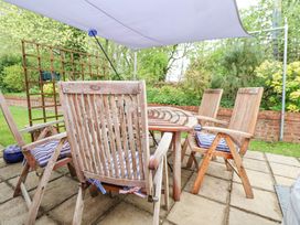 An outdoor patio area with a wooden table surrounded by four wooden chairs with blue and white striped cushions at 2 Mountain View in Chirk