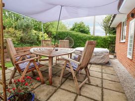 An outdoor patio with a wooden table and chairs under a canopy with a covered hot tub and greenery at 2 Mountain View in Chirk