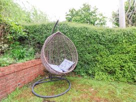 A hanging wicker chair with cushions on grass near a brick wall and hedge at 2 Mountain View in Chirk