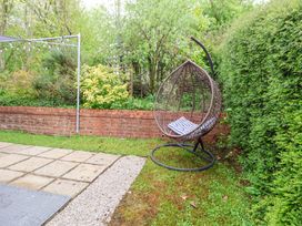 A garden area with a hanging egg chair on grass near a brick wall and hedges at 2 Mountain View in Chirk