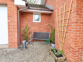 An outdoor corner with a metal bench two potted plants a gravel ground and a wooden planter attached to a brick wall at 2 Mountain View in Chirk