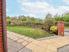 A front garden with grass and shrubs bordered by a brick wall and a paved pathway at 2 Mountain View in Chirk