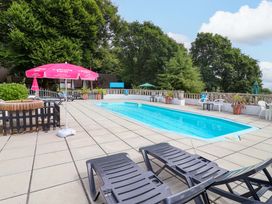 An outdoor swimming pool area with loungers and a parasol at Driftwood - 54 Valley Lodge, St Ann's Chapel, Cornwall