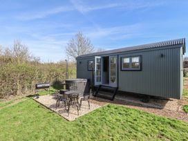 A small gray metal cabin with steps leading to open double doors next to a patio with metal table chairs and a barbecue grill in a grassy yard at Dandelion in Ashby cum Fenby near Waltham