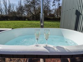 An outdoor hot tub with two glasses of sparkling wine and grass and trees in the background at Dandelion in Ashby cum Fenby near Waltham