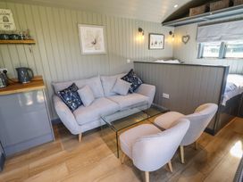 A small living area with a sofa, two chairs, a glass coffee table, and a bed partially visible behind a partition at Dandelion in Ashby cum Fenby near Waltham