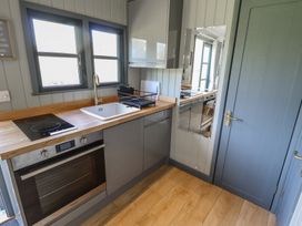 A small kitchen with a sink, stovetop, oven, gray cabinets, wooden countertop, mirror on the wall, and a blue door at Dandelion in Ashby cum Fenby near Waltham