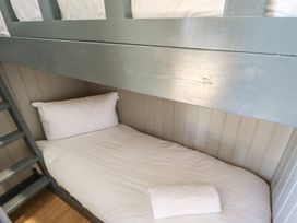 A lower bunk bed with white pillow and rolled towel on white sheets in a room with wood panel walls at Dandelion in Ashby cum Fenby near Waltham