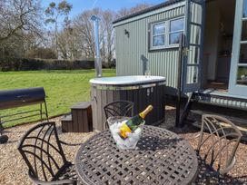 An outdoor seating area with a round metal table and chairs a bottle of champagne in an ice bucket a hot tub small steps and a barbecue grill near a cabin with open doors at Dandelion Ashby cum Fenby near Waltham