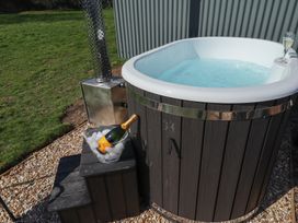 An outdoor hot tub filled with water next to a small step and a bucket with a bottle of champagne on ice at Dandelion in Ashby cum Fenby near Waltham