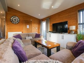 A living room with sofas a wooden coffee table a television on a cabinet and a wall clock at Angel Lodge - No 27 in Fornham St Genevieve near Bury St Edmunds