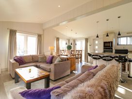 An open living area with sofas, a wooden coffee table, a dining table with chairs, and a kitchen with a breakfast bar and stools at Angel Lodge - No 27 in Fornham St Genevieve near Bury St Edmunds