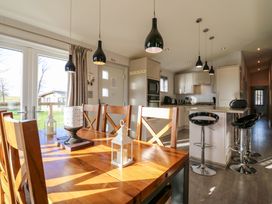 A kitchen and dining area with a wooden dining table and chairs black pendant lights and bar stools at Angel Lodge - No 27 in Fornham St Genevieve near Bury St Edmunds