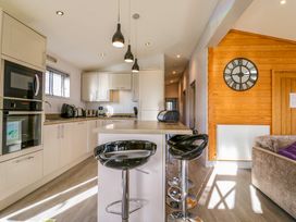 A kitchen with bar stools a clock on a wooden wall and built in appliances at Angel Lodge - No 27 in Fornham St Genevieve near Bury St Edmunds