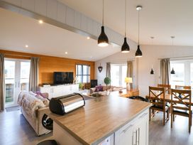An open living and dining area with a kitchen island countertop a sofa a television and a wooden dining table with chairs at Angel Lodge - No 27 in Fornham St Genevieve near Bury St Edmunds