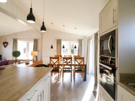A kitchen and dining area with a wooden dining table and chairs under black pendant lights at Angel Lodge - No 27 in Fornham St Genevieve near Bury St Edmunds