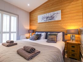 A bedroom with a double bed two bedside tables with lamps and wooden paneled wall at Angel Lodge - No 27 in Fornham St Genevieve near Bury St Edmunds