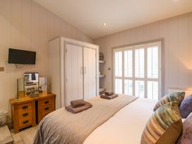 A bedroom with a bed with folded towels pillows a wooden dresser with a mirror a mounted TV white wardrobe and shuttered windows at Angel Lodge No 27 Fornham St Genevieve near Bury St Edmunds
