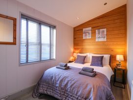 A bedroom with a bed having purple pillows and towels and wooden panel wall at Angel Lodge - No 27 in Fornham St Genevieve near Bury St Edmunds