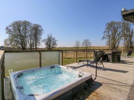 A wooden deck with a hot tub loungers and a table with chairs outside at Angel Lodge - No 27 in Fornham St Genevieve near Bury St Edmunds