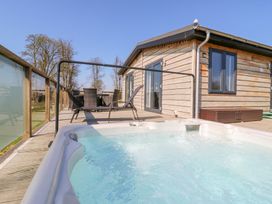 An outdoor deck with a hot tub table and chairs next to a wooden cabin at Angel Lodge - No 27 in Fornham St Genevieve near Bury St Edmunds