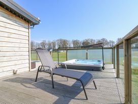 An outdoor wooden deck with a lounge chair and a hot tub with a glass railing at Angel Lodge - No 27 in Fornham St Genevieve near Bury St Edmunds