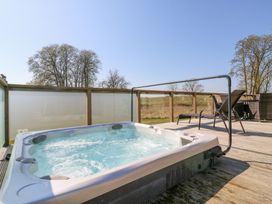 An outdoor hot tub on a wooden deck with lounge chairs and a table surrounded by glass panel fencing at Angel Lodge - No 27 in Fornham St Genevieve near Bury St Edmunds