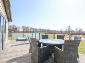 An outdoor deck with a glass table and six wicker chairs and a hot tub in the background at Angel Lodge - No 27 in Fornham St Genevieve near Bury St Edmunds