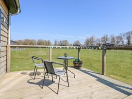 A wooden deck with two chairs a round table and a planter overlooking a grassy field at Angel Lodge - No 27 in Fornham St Genevieve near Bury St Edmunds