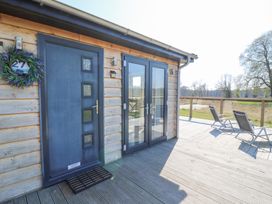 A wooden deck with a blue door and glass double doors next to two lounge chairs at Angel Lodge - No 27 in Fornham St Genevieve near Bury St Edmunds