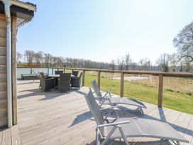 A wooden deck with outdoor chairs and table overlooking grassy fields and trees at Angel Lodge No 27 in Fornham St Genevieve near Bury St Edmunds