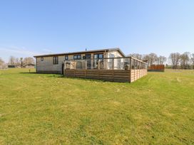 A wooden house with a glass railing deck on a grassy field at Angel Lodge - No 27 in Fornham St Genevieve near Bury St Edmunds