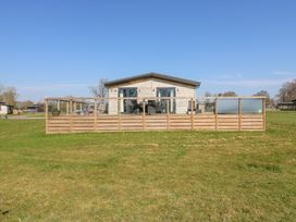 A wooden cabin with a fenced patio on a grassy field at Angel Lodge - No 27 in Fornham St Genevieve near Bury St Edmunds