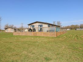 A wooden lodge with a deck and outdoor furniture on a grassy field at Angel Lodge - No 27 in Fornham St Genevieve near Bury St Edmunds