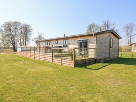 A wooden cabin with glass-paneled fenced deck in a grassy area with trees at Angel Lodge - No 27 in Fornham St Genevieve near Bury St Edmunds