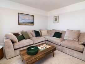 A living room with a beige corner sofa with green and beige cushions a wooden coffee table with books and decor and paintings on the wall at Combe View in Ilfracombe