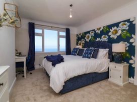 A bedroom with a double bed featuring white bedding and blue cushions against a floral wallpaper and a window overlooking the sea at Combe View in Ilfracombe
