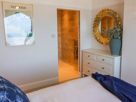 A bedroom with a bed a dresser with a round mirror and a vase next to an open door to a tiled bathroom at Combe View in Ilfracombe
