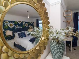 A bedroom with a bed reflected in a gold round mirror and a vase with flowers on a white table at Combe View in Ilfracombe