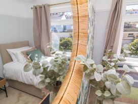 A bedroom with a single bed with pillows near two windows and a plant reflected in a curved mirror at Combe View in Ilfracombe
