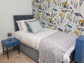 A bedroom with a single bed with pillows and a blanket next to blue bedside tables and a wallpaper with bird and leaf patterns at Combe View in Ilfracombe