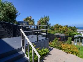 An outdoor garden area with stairs leading to a deck and plants with trees and a shed in the background at Combe View in Ilfracombe
