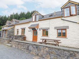 The exterior of a stone cottage with wooden framed windows a wooden door and a picnic table at Llys-y-Wennol in Penmachno