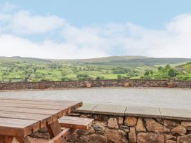 A wooden picnic table on a stone patio overlooking a stone wall and green hills at Llys-y-Wennol in Penmachno