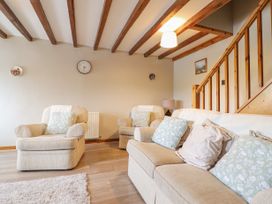 A living room with beige armchairs and sofa with cushions wooden beams on ceiling and wooden staircase at Llys-y-Wennol in Penmachno