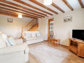 A living room with two beige sofas a wooden staircase a wooden tv cabinet with a television a wooden side table with a lamp and a rug on the floor at Llys-y-Wennol in Penmachno
