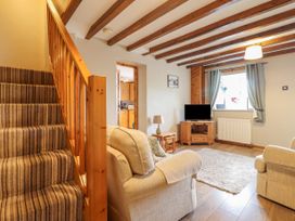 A living room with beige sofas a wooden staircase a television on a wooden cabinet and a window with curtains at Llys-y-Wennol in Penmachno