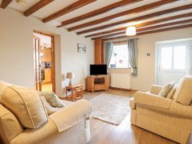 A living room with two beige sofas a wooden TV stand with a television a small table with a lamp and a window with curtains at Llys-y-Wennol in Penmachno