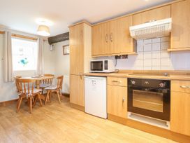 A kitchen with wooden cabinets a microwave oven a small refrigerator a dining table with four chairs and a window at Llys-y-Wennol in Penmachno