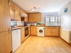 A kitchen with wooden cabinets a washing machine a microwave a toaster and a window at Llys-y-Wennol in Penmachno